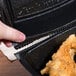 A hand holding a Dart black foam container with fried chicken inside.