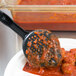 A black plastic Vollrath Spoodle with a black handle on a plate of meatballs with red sauce.
