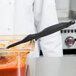 A person in a white coat using a Vollrath High Heat Perforated Spoodle in a container of red sauce.
