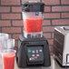 A Waring commercial blender filled with red liquid on a metal counter.