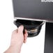 A hand using a Bunn black container to fill a coffee cup.