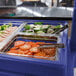 A navy blue Cambro buffet and salad bar tray with a variety of food on it.