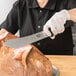A person using a Victorinox Butcher Knife to cut ham on a counter.