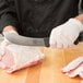 A person in gloves using a Victorinox beef skinning knife to cut meat on a cutting board.