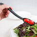 A hand using a Cambro black solid salad bar spoon to serve tomatoes onto a salad.