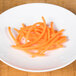 A plate of julienned carrots on a wooden surface.
