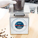 A person wearing a glove weighing coffee beans on a white and blue Edlund portion scale.