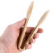 A hand holding a pair of beige plastic tongs.