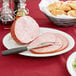A Tuxton bright white china platter with sliced ham and a fork.