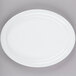 A Tuxton bright white narrow rim oval china platter on a gray surface.