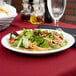 A close-up of a Tuxton Colorado narrow rim bright white china plate with salad on a table.