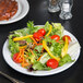 A plate of salad with yellow peppers and tomatoes on a Tuxton Colorado narrow rim plate.