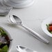 A white table with a Visions silver plastic serving fork and a bowl of salad.