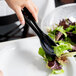 A person using black Visions plastic tongs to serve salad at a table.