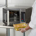 A chef in a white coat using a Solwave commercial microwave to heat a tray of food.