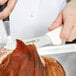 A person using a Dexter-Russell Sani-Safe Lamb Skinning Knife with a white handle to cut meat on a counter.