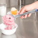 A hand holding a Zeroll TubMate Ice Cream Spade over a bowl of pink ice cream.