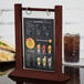 A Menu Solutions mahogany wood flip top table tent with a drink on a table.