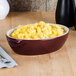 A Tuxton burgundy and eggshell oval bowl filled with macaroni and cheese.