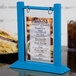 A Menu Solutions wood table tent with a menu on a table holding a sandwich.