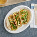 An EcoChoice bagasse oval platter with two tacos on a table.