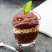 A triangle dessert glass filled with chocolate pudding with nuts and mint.