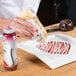 A hand using a Smucker's Platescapers bottle to drizzle cream on a white plate with red and white sauce drizzled on it.