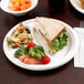 A white EcoChoice Compostable Sugarcane plate with a sandwich and vegetables on it.