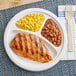 A EcoChoice Compostable Sugarcane Bagasse 3 Compartment Plate with grilled chicken, beans, and corn.