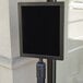 A black Aarco stanchion sign frame with white border on a pole.