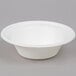 A close up of an EcoChoice Compostable Sugarcane bowl with a white rim on a gray background.
