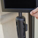 A person using a black Aarco stanchion sign frame to display a black tablet.