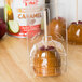 A large disposable plastic bubble for a caramel apple on a plastic container with a piece of candy in it.