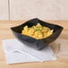 A black Fineline plastic bowl filled with macaroni and cheese on a white surface.