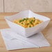 A white Fineline plastic bowl filled with macaroni and cheese on a white table.