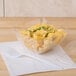 A Fineline clear plastic bowl filled with macaroni and cheese on a school kitchen counter.