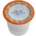 A white Caffe de Aroma single serve coffee cup with orange and brown text and lid that says "Decaf Hazelnut"