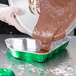 A hand wearing a plastic glove pouring brown liquid into a Durable Packaging Christmas Tree foil pan.