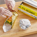 A hand in a plastic glove wrapping a sandwich in Choice gold and silver foil sheets.