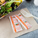 A salad in a bowl with a white shade and French dressing packets next to a fork.