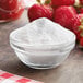 A bowl of white powder next to strawberries.