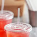 A plastic cup with a Choice jumbo clear straw in a red drink with a lid.