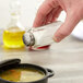 A hand holding a Tablecraft flat paneled salt shaker over a bowl of soup.