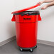 A person putting a lid on a red Continental Huskee trash can.