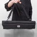A person holding a Mercer Culinary black knife roll bag with a strap.
