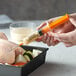 A hand using a Cajun Injector syringe to inject yellow marinade into a piece of chicken.