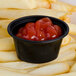 A close up of a black Newspring oval plastic souffle cup with ketchup in it.