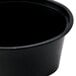 A black Newspring oval plastic souffle cup with a black lid.