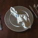 A Tabletop Classics silver plastic charger plate with a white napkin on it.
