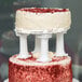 A close up of a red velvet cake on a Wilton scalloped edge cake separator plate with white columns.